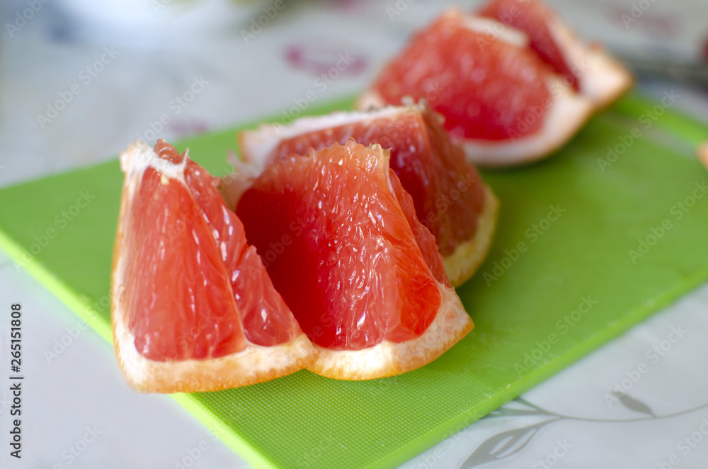 Slices of fresh, juicy grapefruit are on a green desk Slices of fresh, juicy grapefruit are on a green desk