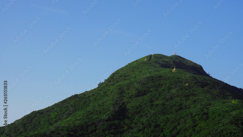 Beautiful scenery of green forest mountain scape and clear blue sky with small temple shelters on top of the mountain.