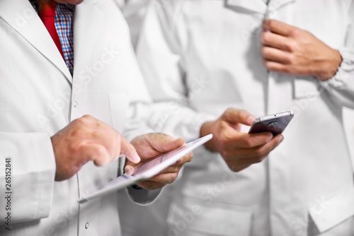 Employees confer stand in white coats using a tablet computer and telephone.