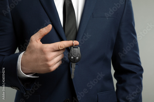 Young man holding car key on grey background, closeup