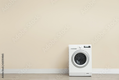 Washing machine near color wall in empty room, space for text. Laundry day