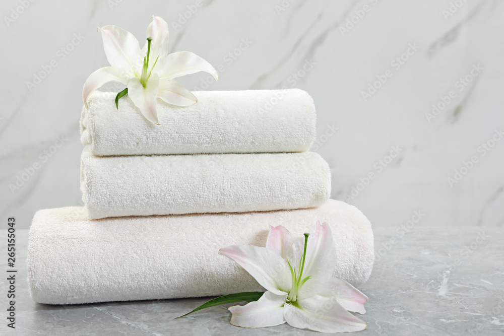 Stack of fresh towels with flowers on grey table against light background. Space for text
