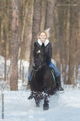 A young woman riding a black horse in snowy forest