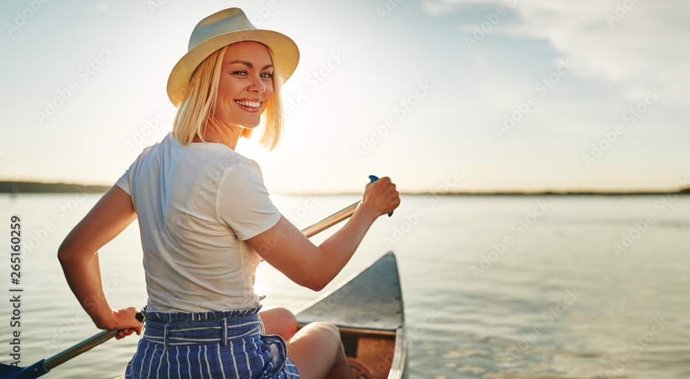 Smiling young woman canoeing on a lake in summer - obrazy, fototapety, plakaty 