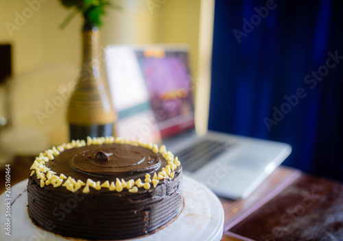 Dark chocolate cake with chocolate frosting and white chocolate chips with a computer in the background