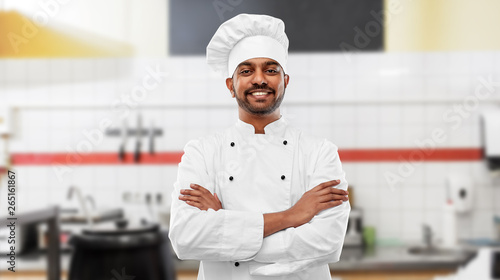 cooking, profession and people concept - happy male indian chef in toque with crossed arms over restaurant kitchen background photo