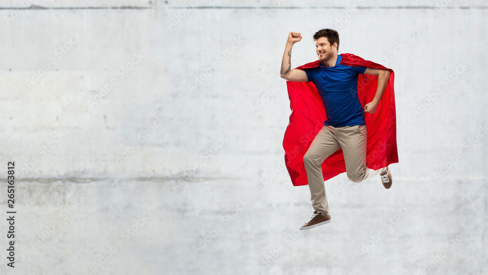 super power and people concept - happy young man in red superhero cape jumping in air over grey concrete background super power and people concept - happy young man in red superhero cape jumping in air over grey concrete background