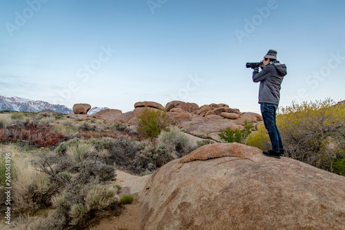 Asian man photographer and tourist holding DSLR camera taking photo of abstract rock landscape at Alabama Hills, Lone Pine, California, USA. Travel photography concept