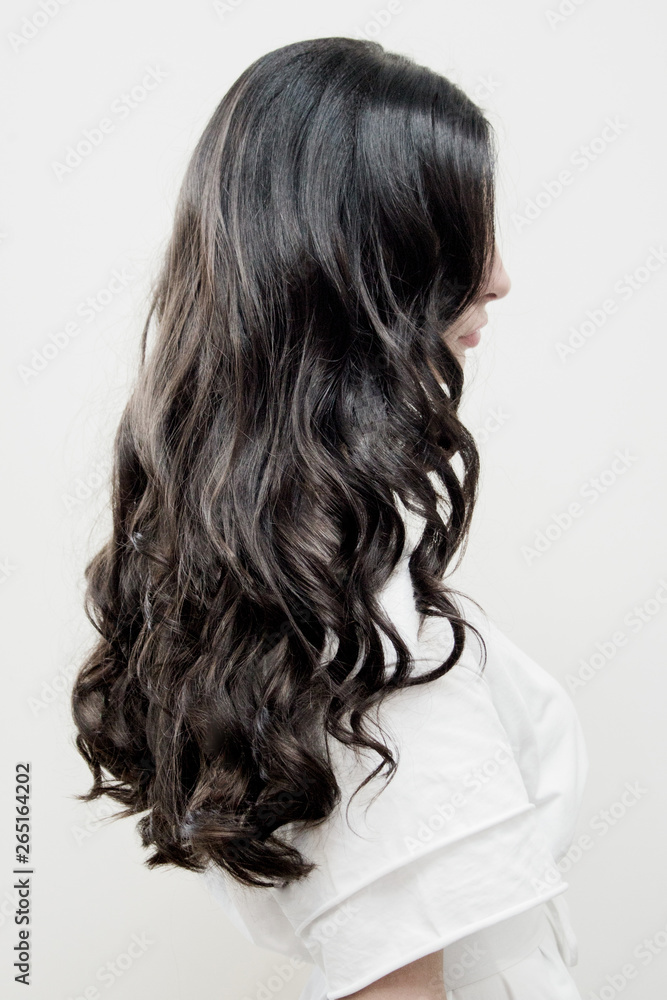 Naklejka premium Black long hair of a girl from a back against a white wall