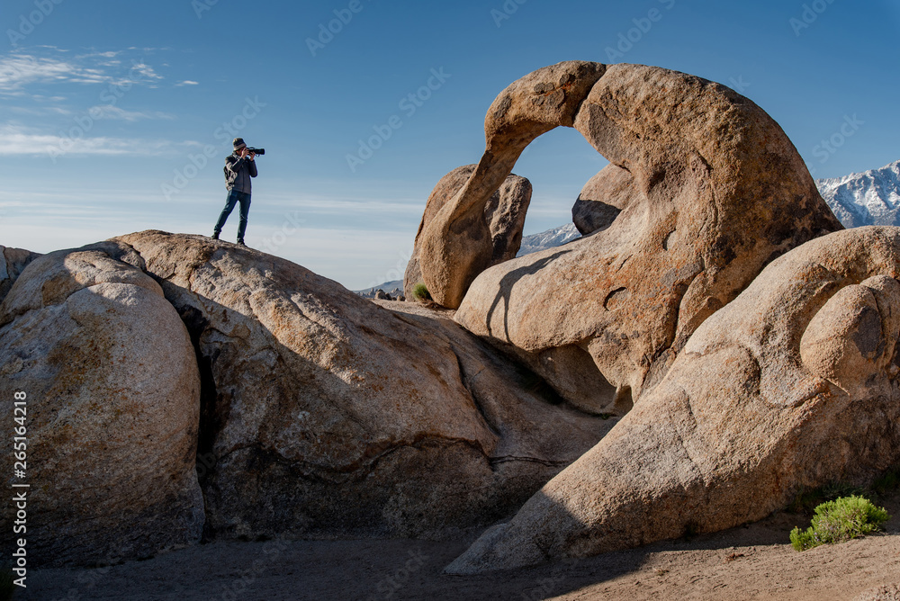 Asian man photographer and traveler holding camera taking photo through the mobius arch stone at Alabama Hills, Lone pine, USA. Travel photography concept