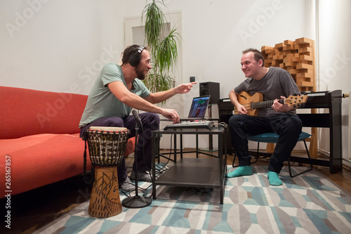 Two musicians playing instruments in home music studio.