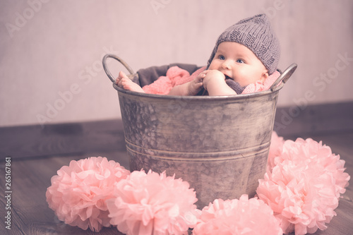 Portrait süßes Baby sitzt im Eimer mit Mütze rosa Ponpons