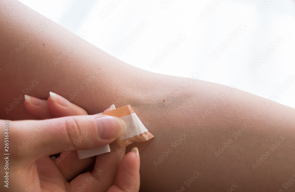woman removing adhesive plaster off injury after blood test injection