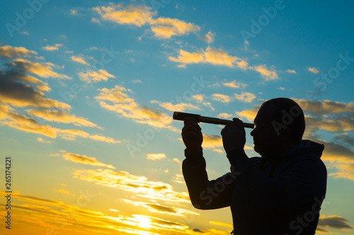 Silhouette of a man with a spyglass on the background of a dramatic sky in the sunset. Conceptt look at the future, pry, travel photo