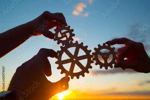 hands of businessmen assemble a puzzle from gears against the sky in the sunset. business concept idea, partnership, innovation, teamwork, cooperation