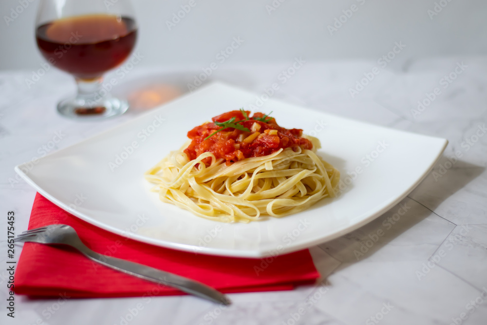 Pasta with fresh tomatoes, cooked with olive oil and garlic on a light background and a white square plate. Italian food. Horizontal orientation