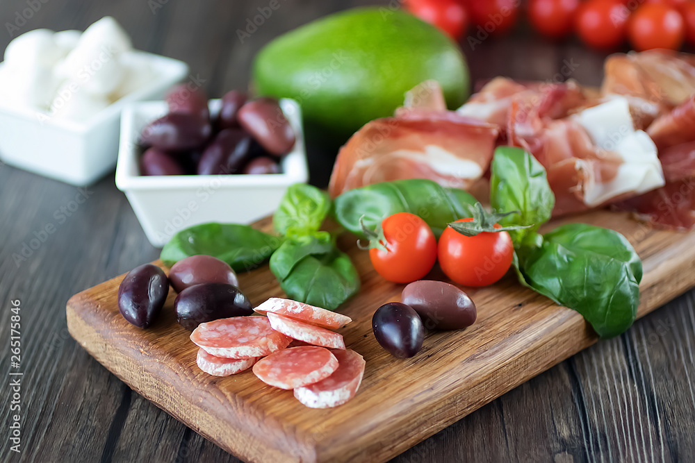 Prosciutto, bread, olives, walnut, mozzarella, salami, basil and cherry tomatoes on brown wooden board. Mediterranean kitchen. Prosciutto, bread, olives, walnut, mozzarella, salami, basil and cherry tomatoes on brown wooden board. Mediterranean kitchen.