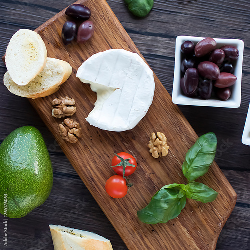 Camembert cheese, bread, olives, walnut, mozzarella,basil and cherry tomatoes on  brown wooden board.  Mediterranean kitchen.