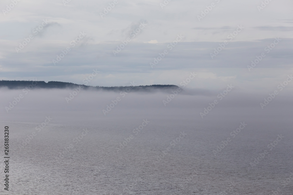 Beautiful atmospheric early morning landscape with mist rising over the St. Lawrence Gulf waters in a northern Anticosti Island bay, with a cape in the background