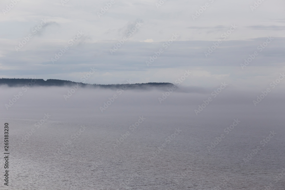 Beautiful atmospheric early morning landscape with mist rising over the St. Lawrence Gulf waters in a northern Anticosti Island bay, with a cape in the background Beautiful atmospheric early morning landscape with mist rising over the St. Lawrence Gulf waters in a northern Anticosti Island bay, with a cape in the background