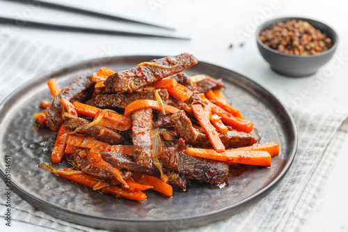 Close-up of Chinese spicy Szechuan beef meal on a black plate with wooden sticks over white table. Asian food recipe; portion for one person.