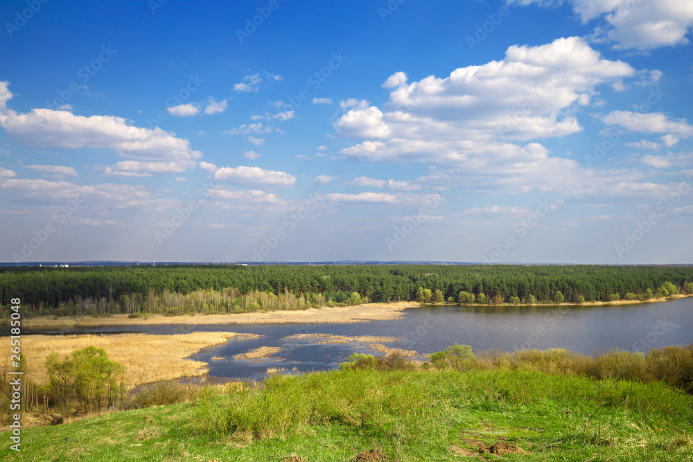 Beautiful view of river, green forest and blue cloudy sky from the top of the hill. Spring landscape.