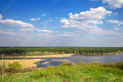 Beautiful view of river  green forest and blue cloudy sky from the top of the hill. Spring landscape.