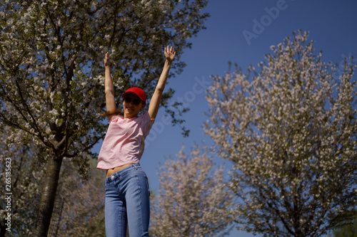 Successful business woman enjoys her leisure free time in a park with blossoming sakura cherry trees wearing jeans  pink t-shirt and a fashion red cap