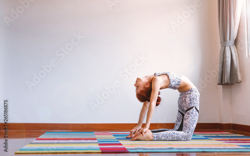 Full length young attractive woman practicing yoga in Ustrasana exercise, carmel pose workout on mat at home. exercise fitness, healthy lifestyle concept. photo