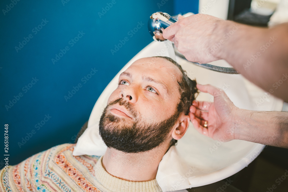Barbershop theme. Hairdresser for washing hair in a barbershop. Hands male hairdresser close-up washes hair with foam and shampoo Caucasian man with beard Barbershop theme. Hairdresser for washing hair in a barbershop. Hands male hairdresser close-up washes hair with foam and shampoo Caucasian man with beard