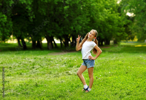A charming girl in shorts and a t-shirt smiles in the summer against the green in the park