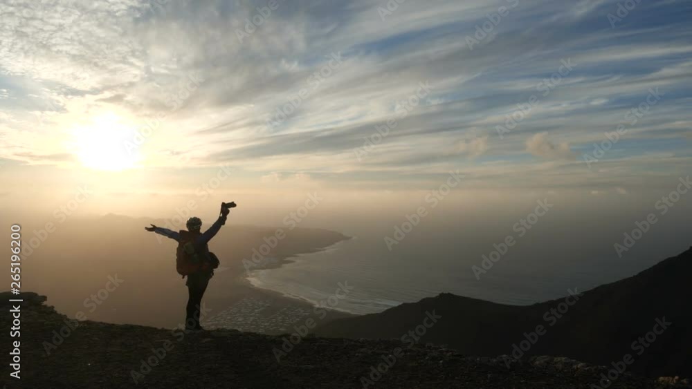 Silhouette of a girl in bicycle helmet with backpack taking pictures of an incredible sunset on the top of a Mountain above the ocean on Canary Islands. Lanzarote. Silhouette of a girl in bicycle helmet with backpack taking pictures of an incredible sunset on the top of a Mountain above the ocean on Canary Islands. Lanzarote.