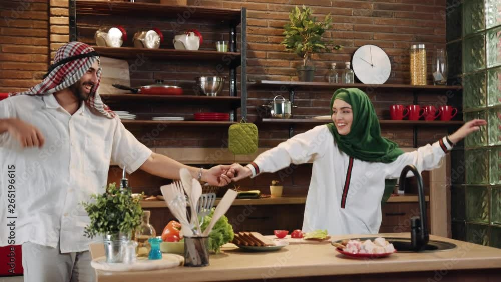 Funny young muslim couple cook together cut vegetables dance on kitchen