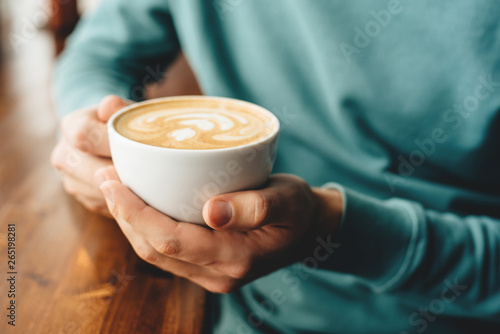 A man in a blue jumper holding a cup of cappuccino in his hands during breakfast