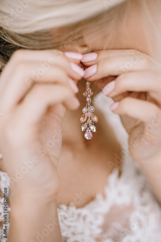 Elegant blonde bride putting on earrings closeup, preparing for wedding