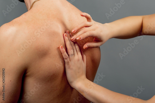Close-up of naked man's body and female's hands checking back. Doctor's hands examine the man with back pain on the gray background.
