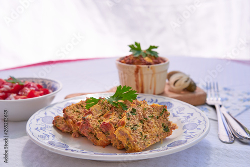 Baked egg pie or kind of quiche, french style dish served on rustic plate with fresh tomato salad. Made from eggs, smoked ham, parsley, pork meat and bread. Traditional spring food in Czech Republic.