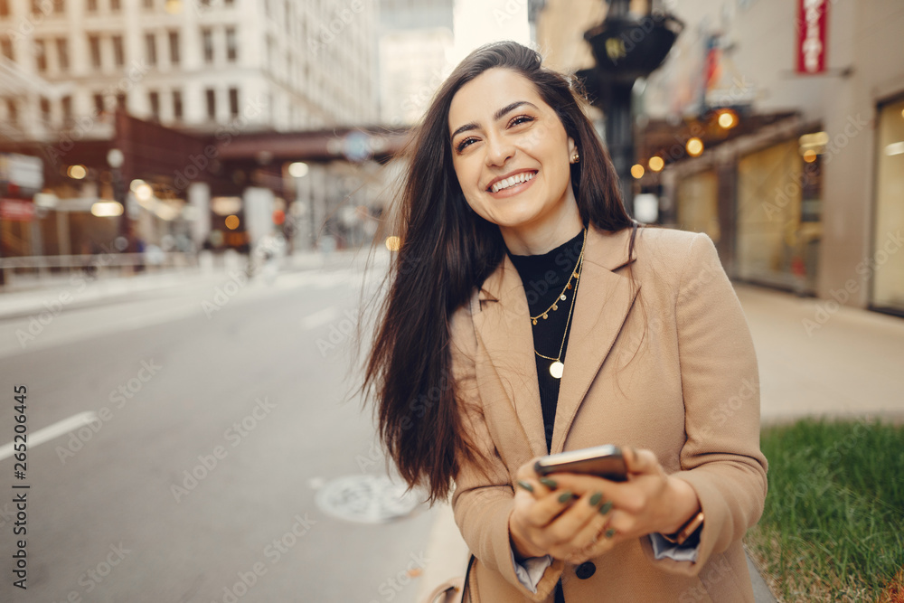 Fototapeta premium Beautiful girl in a city. Stylish brunette in a brown coat. Woman in a Chicago. Lady with a phone