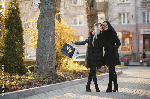 two stylish and luxurious girls walking in the autumn city with shopping bags