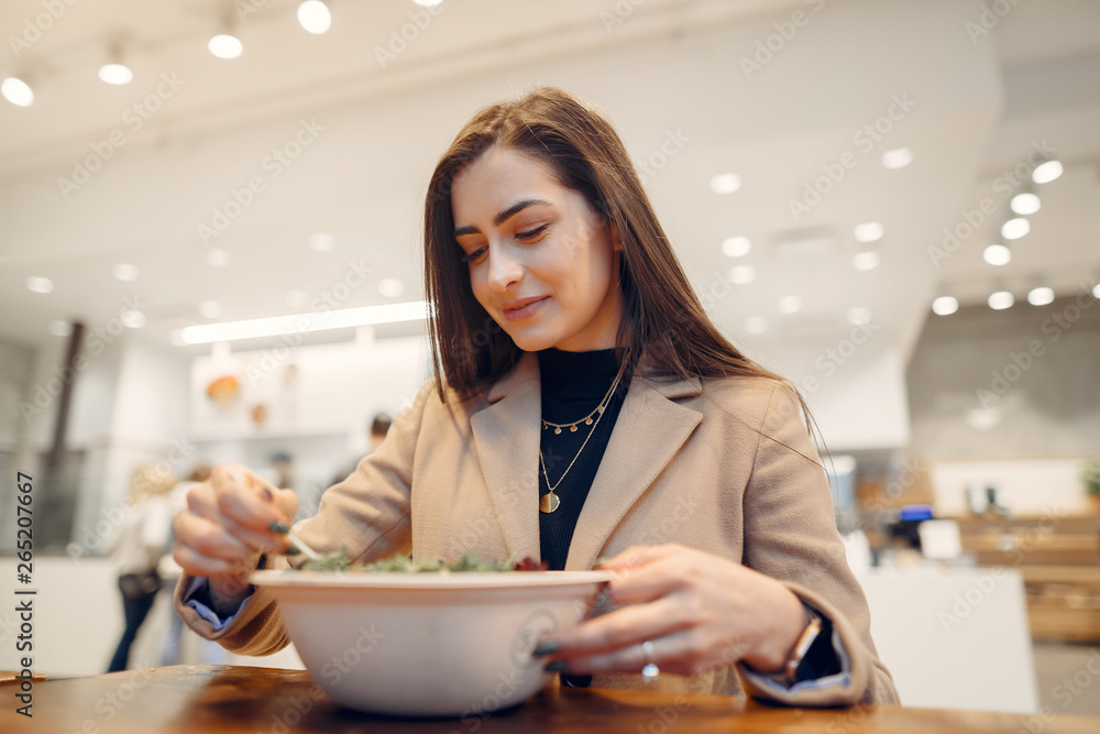 Girl eats vegetable salad. Lady sitting in a cafe. Brunette in a brown coat Girl eats vegetable salad. Lady sitting in a cafe. Brunette in a brown coat