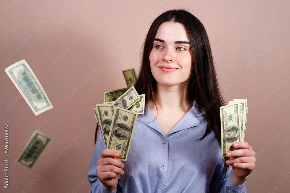 Charming positive successful lucky cheerful woman standing under shower from money having a lot of dollar bills in hands
