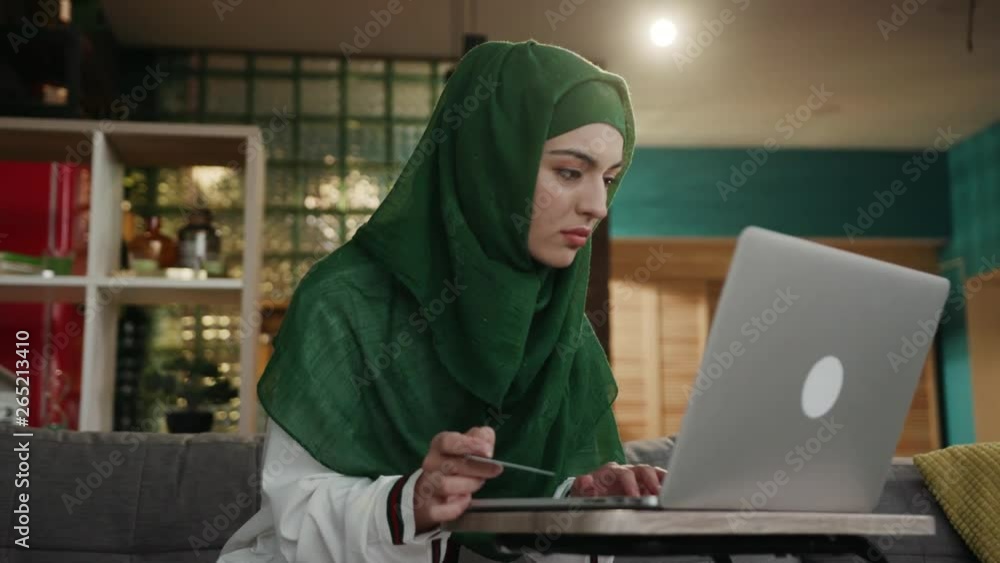 Close up view of pretty young muslim woman shopping online, entering card number on laptop, transaction. Relaxation, money, successful lifestyle. Surfing the internet, gadgets and devices concept Close up view of pretty young muslim woman shopping online, entering card number on laptop, transaction. Relaxation, money, successful lifestyle. Surfing the internet, gadgets and devices concept