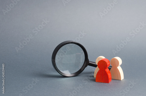 Obraz na plátně Three wooden human figure stands near a magnifying glass on a gray background