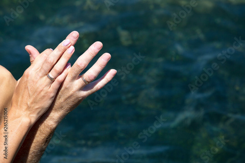 hands of the newlyweds, with wedding gold rings, against the background of the blue sea