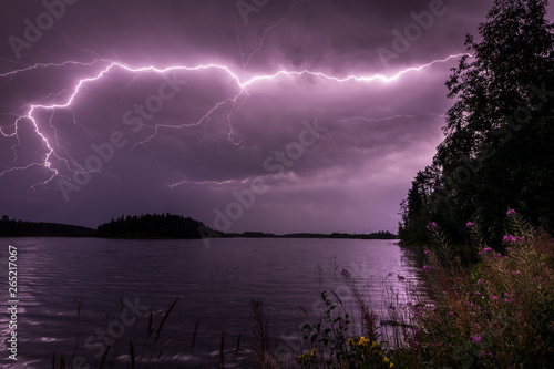 Purple lightning streak through clouds over water photo