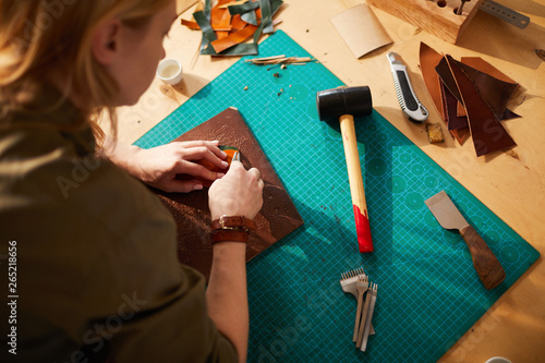 High angle portrait of female artisan making leather bag in atelier lit by sunlight, copy space