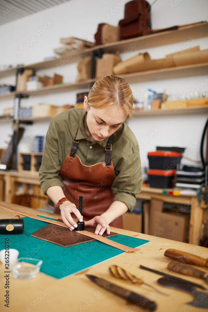 Waist up portrait of female artisan measuring leather piece in workshop, copy space Waist up portrait of female artisan measuring leather piece in workshop, copy space