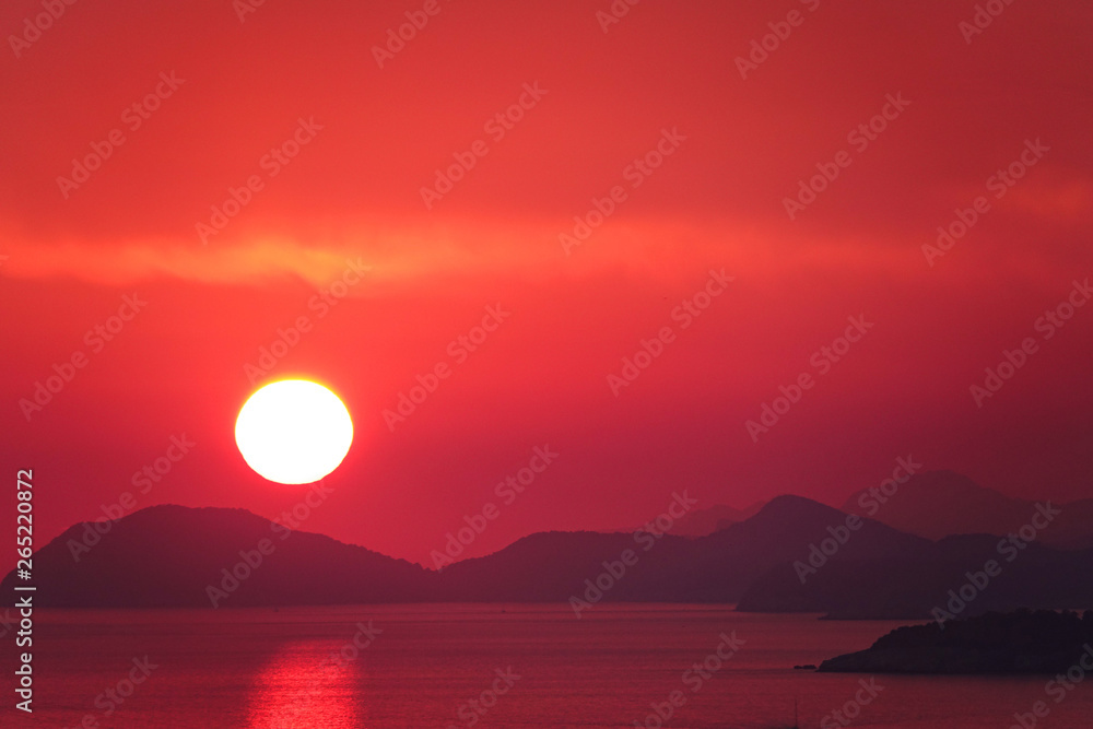 AERIAL Flying towards orange sun descending behind the peaceful island landscape