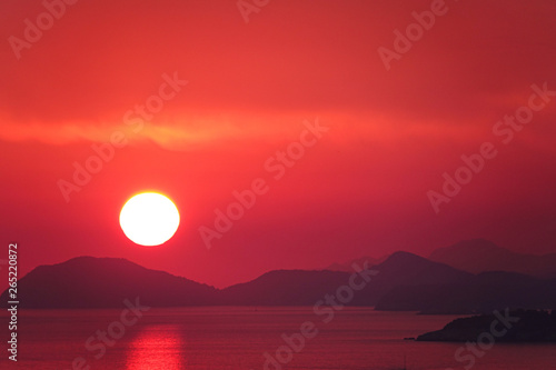 AERIAL Flying towards orange sun descending behind the peaceful island landscape