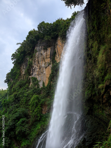 Waterfall  Mountain Cliffs and Green Trees in Background. Vertical Portrait Photograph  Powerful torrential water falling over the edge of cliffs